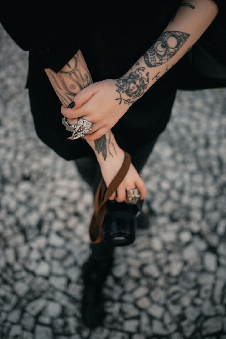 Tattooed hands holding a camera with a strap.