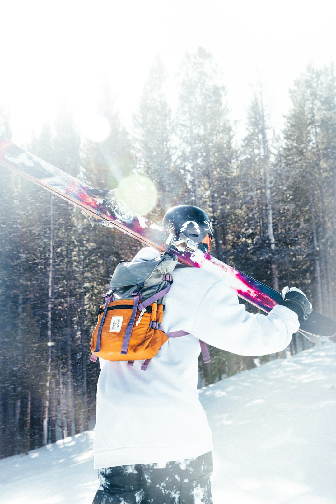 Skier walks through snow with skis over shoulder.